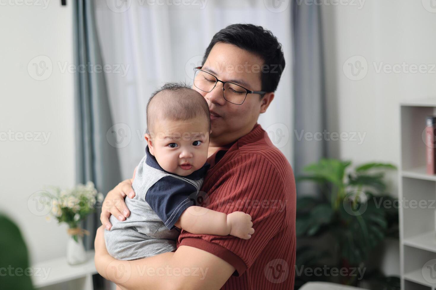 Asian single father stands holding his young son tenderly and lovingly in a cozy living room at home. Cute moment between father and son photo