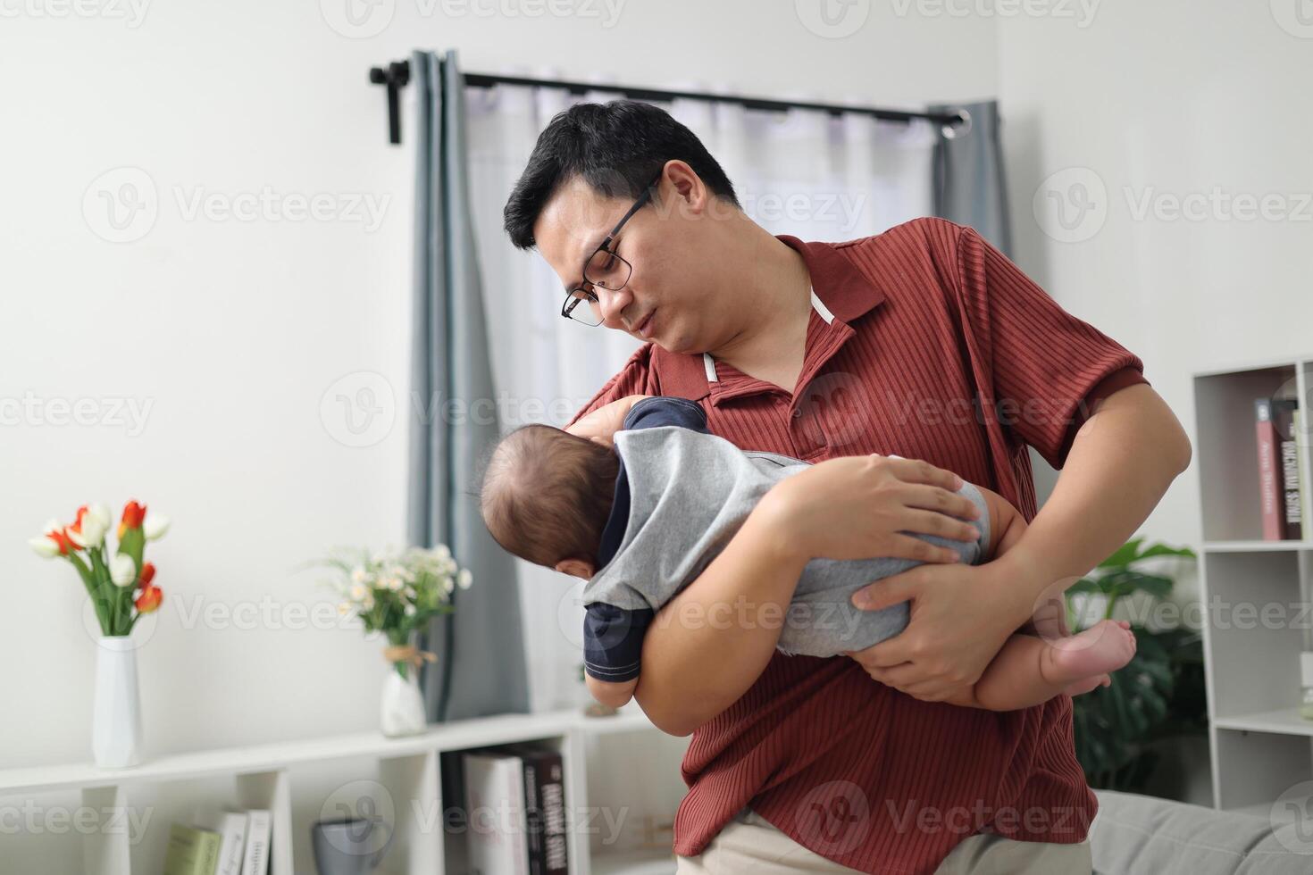 Portrait of Asian father wearing casual striped polo shirt holds little son and plays with him happily in a cozy room at home. Cute moment between father and son photo