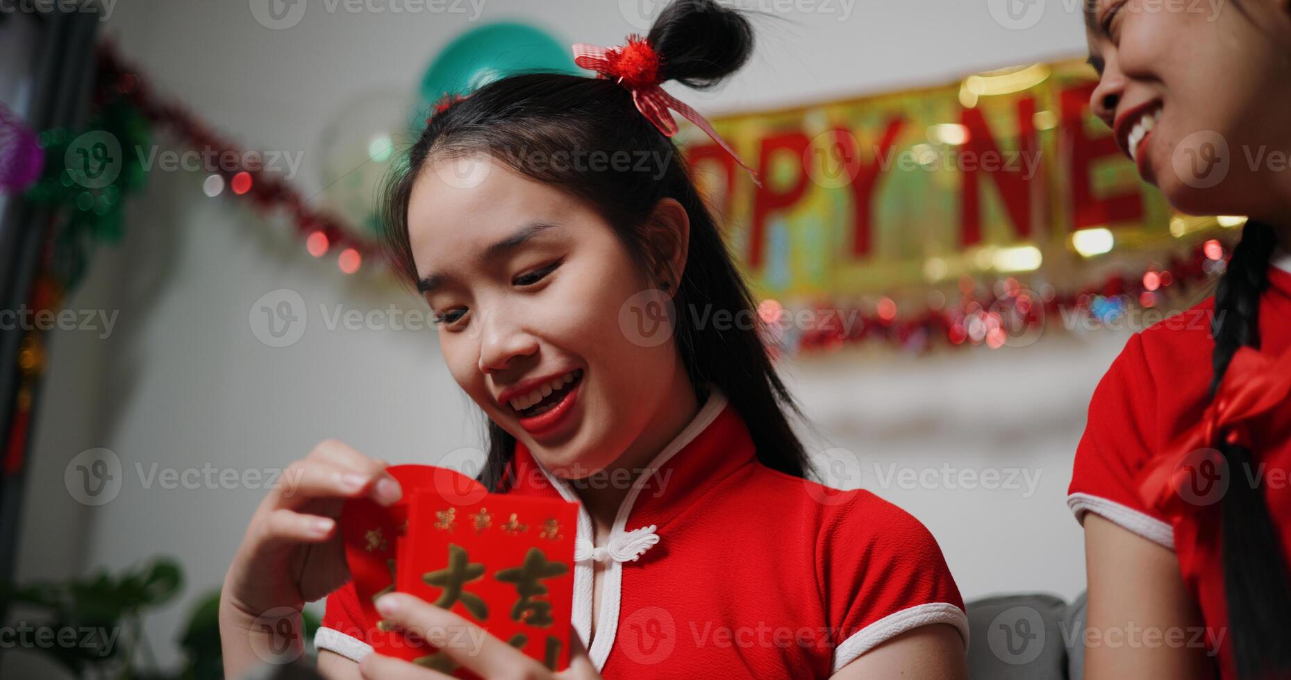 Happy Asian mother gives red envelope gift to daughter with blessing on sofa in living room at home photo