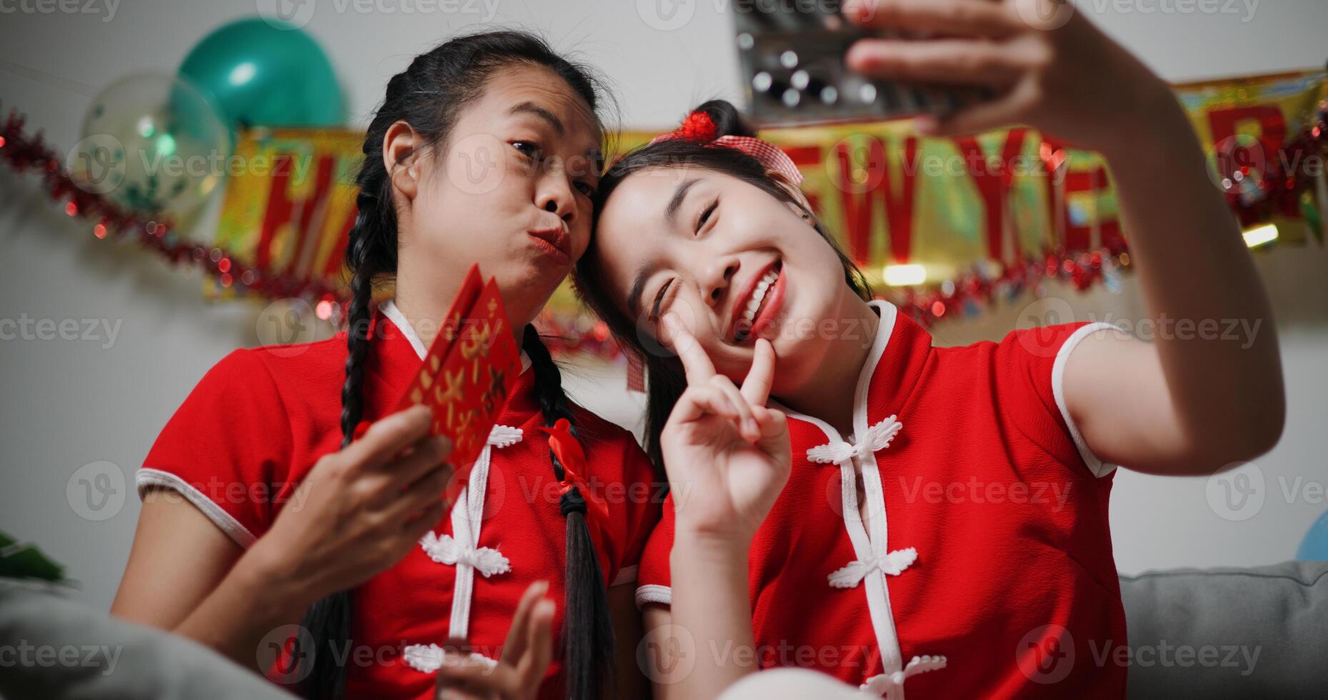 Asian mother and daughter sitting on sofa and using mobile phone to take selfie together in living room at home. Asian family celebrating Lunar New Year together. photo