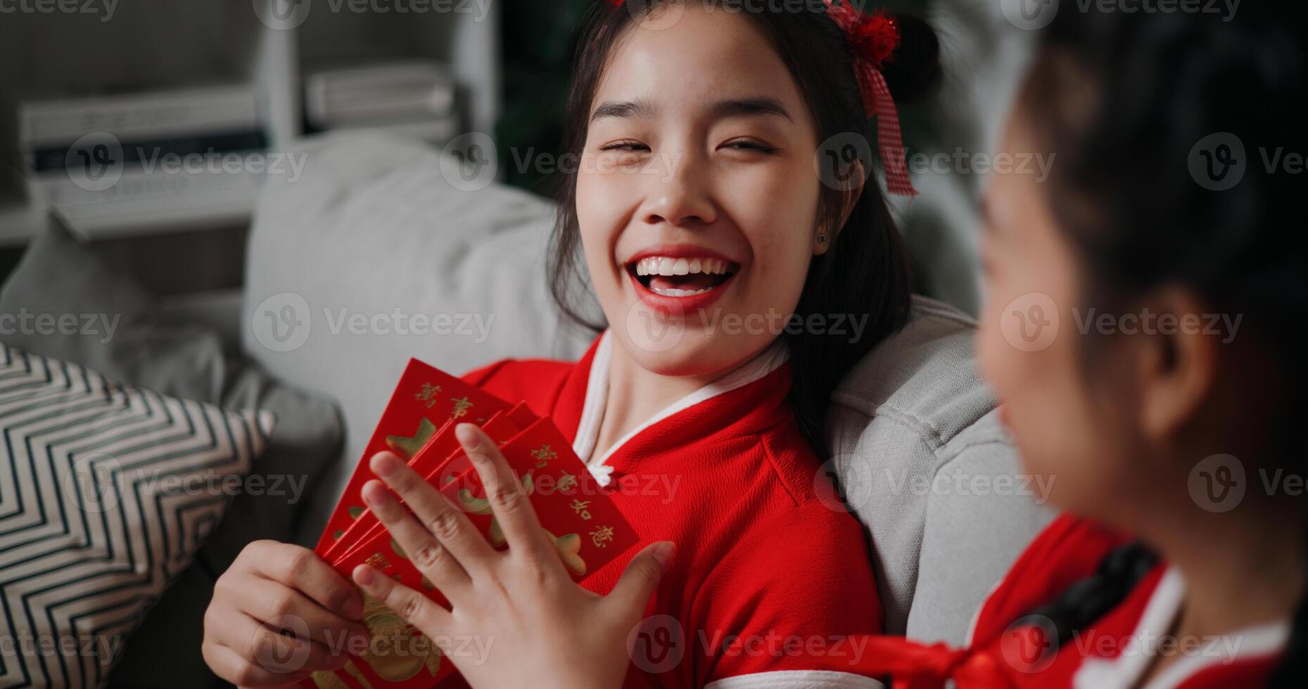 Selective focus shot, Cheerful young woman is holding a red envelope and chatting happily with her mother in the cozy living room. Asian family celebration Lunar New Year together photo