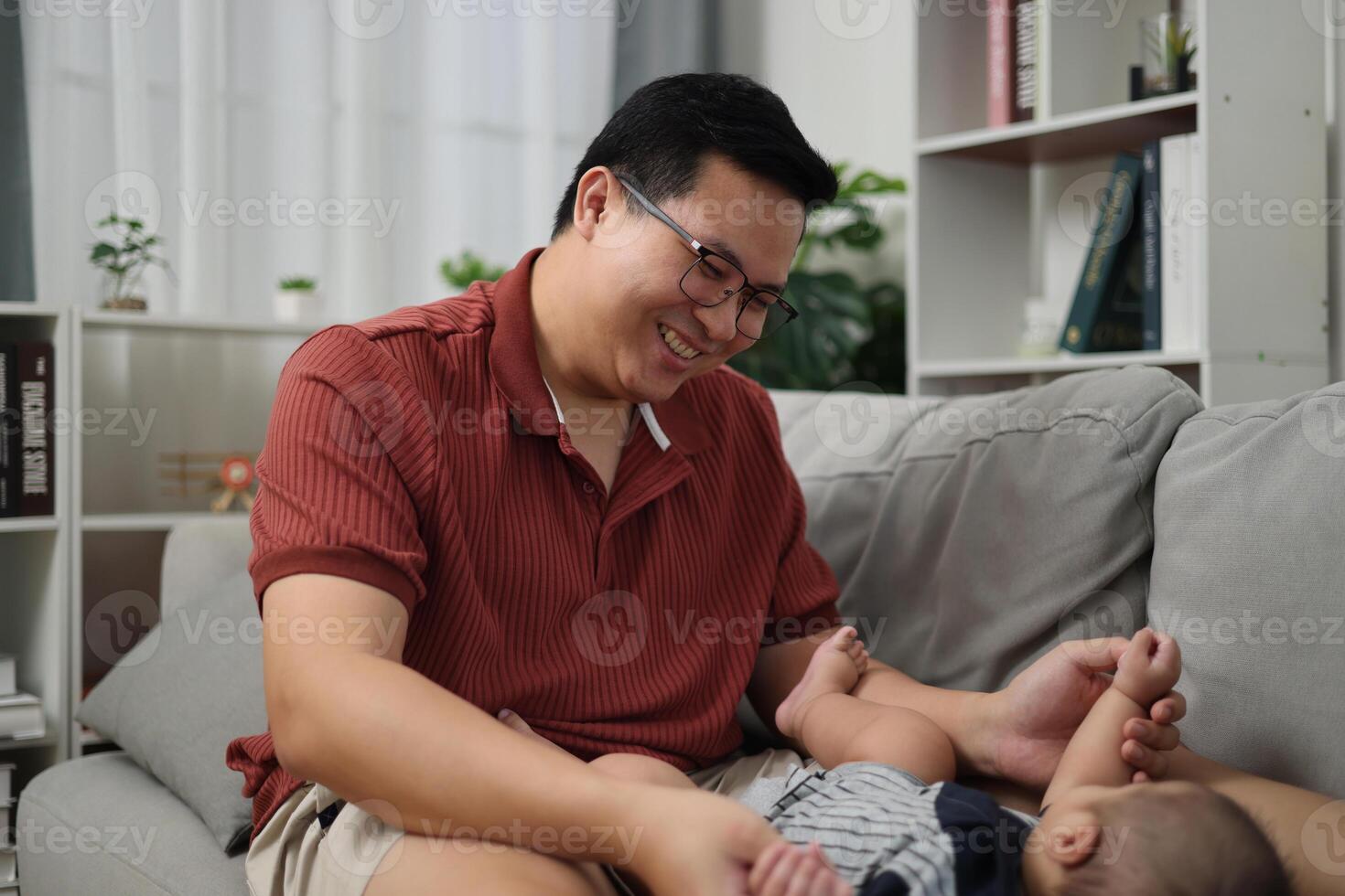 Portrait of Asian father is having fun playing with little son on the sofa in the living room at home with a warm and loving atmosphere. Happy family life. photo