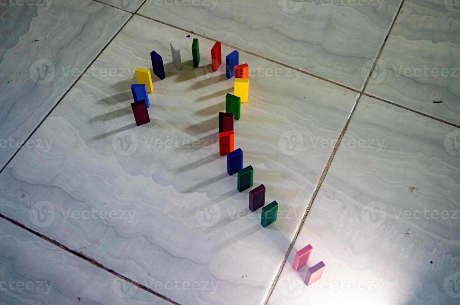 The Colorful dominoes arranged in a question mark shape on a tiled floor, casting shadows. This creative setup is visually striking and thought provoking photo