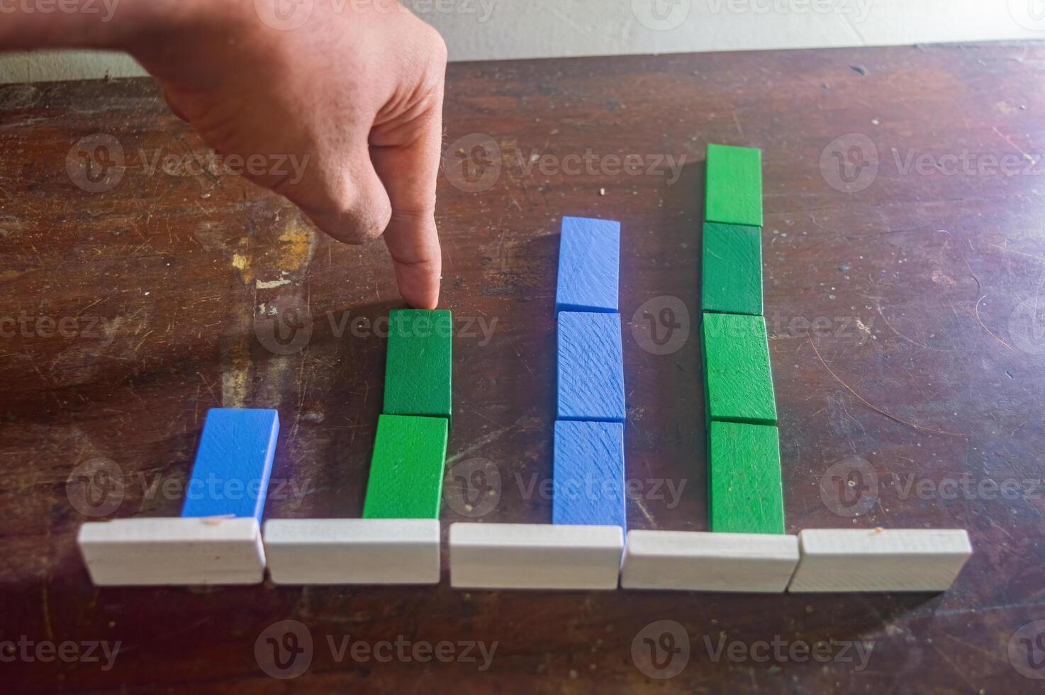 A hand points to a colorful bar chart made of wooden blocks on a wooden surface, illustrating data comparison in a simple and engaging way photo