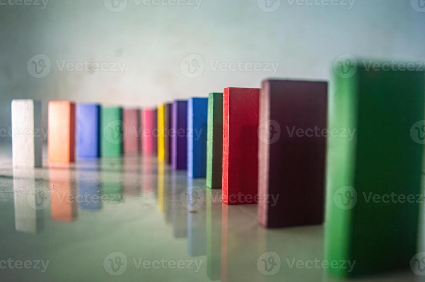 Colorful wooden blocks arranged in a row, creating a visually appealing pattern. The blocks are standing upright on a reflective surface, showcasing various vibrant colors photo