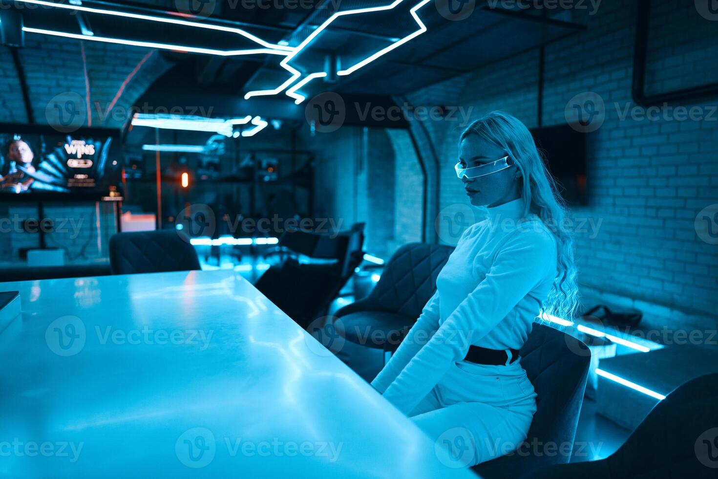 Neon blue light falls on a young woman wearing futuristic glass glasses. photo