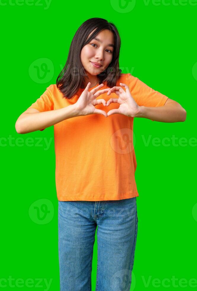Young person makes heart shape with hands against bright green background during casual indoor setting photo