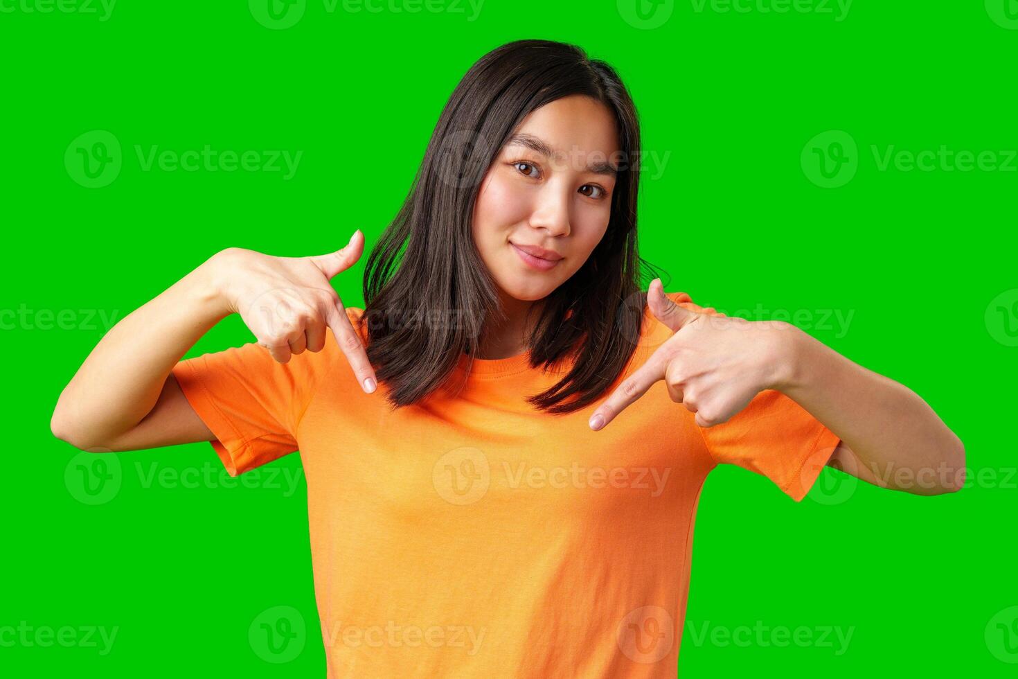 Young woman in orange shirt pointing at blank space against bright green background for creative or promotional purposes photo