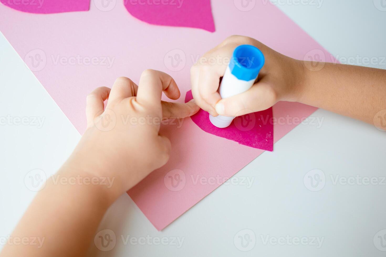 Child crafting with pink and blue supplies on a white table photo