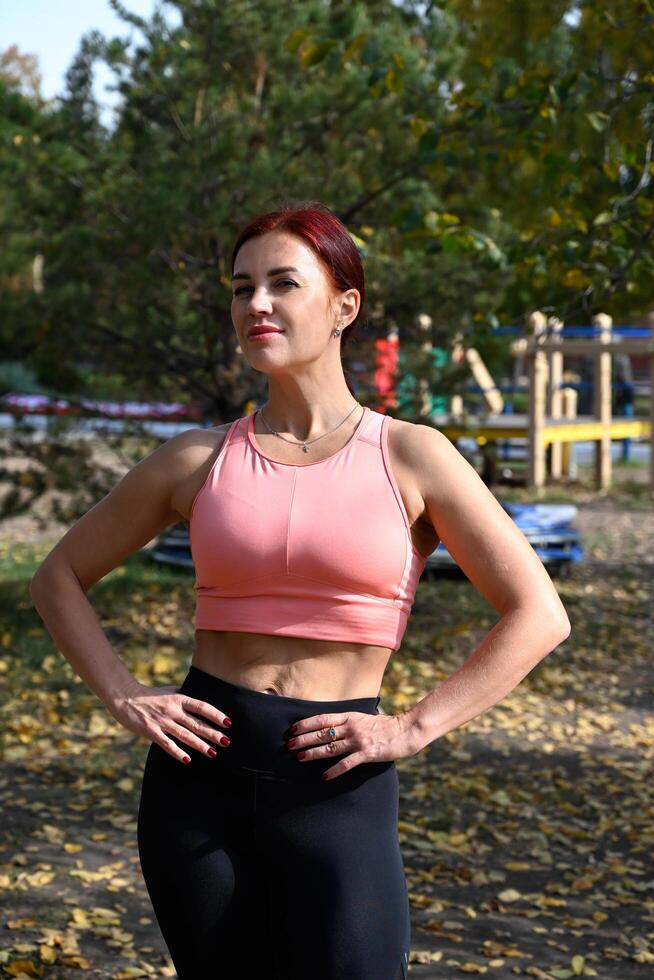A moment captured of a woman's fitness journey, posing amidst a park's autumnal beauty, possibly before or after a workout photo