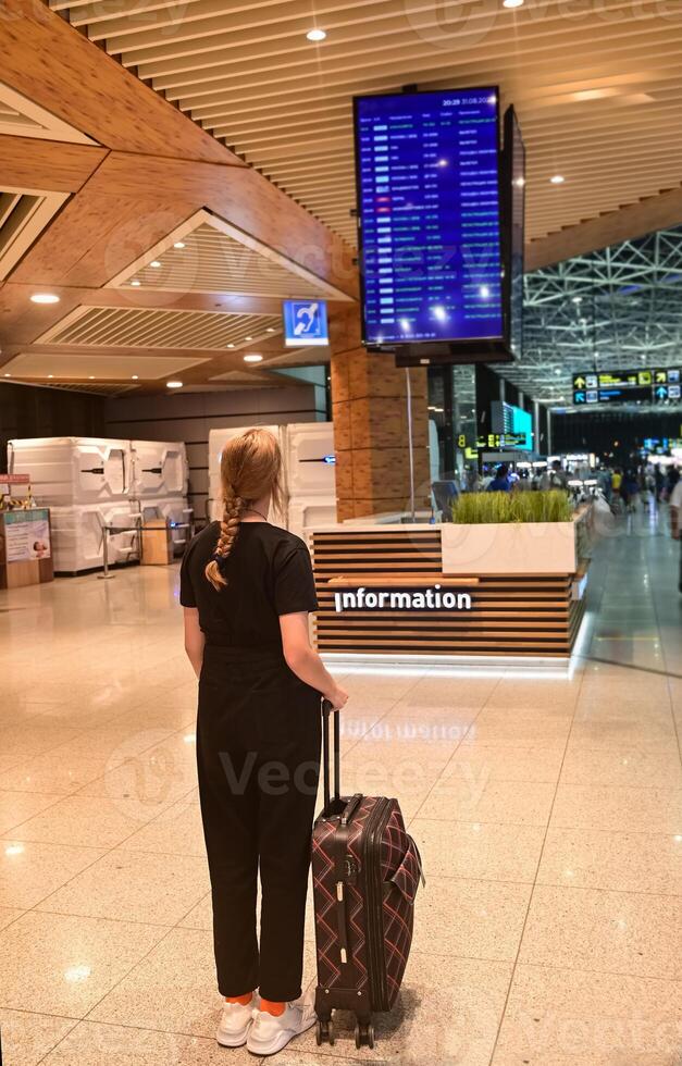 On a beautiful sunny morning Faceless girl in green coat holds passport with ticket and yellow suitcase airport. Airplane travel concept. photo