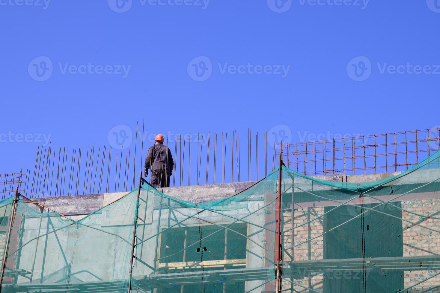 The image portrays a building under construction, with a worker visible on the upper level, highlighting the work in progress photo