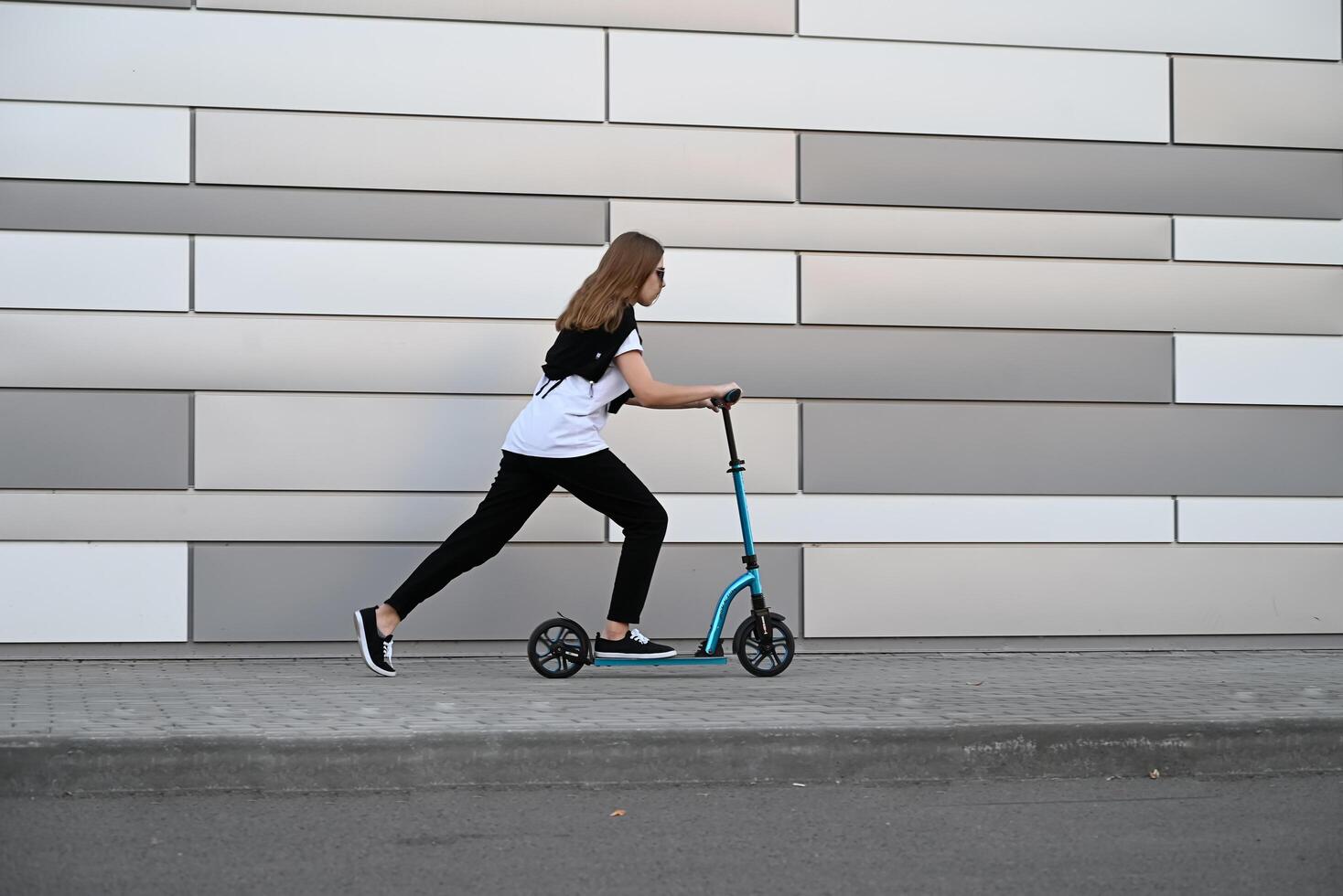A person is riding a blue scooter in front of a modern, paneled wall. photo