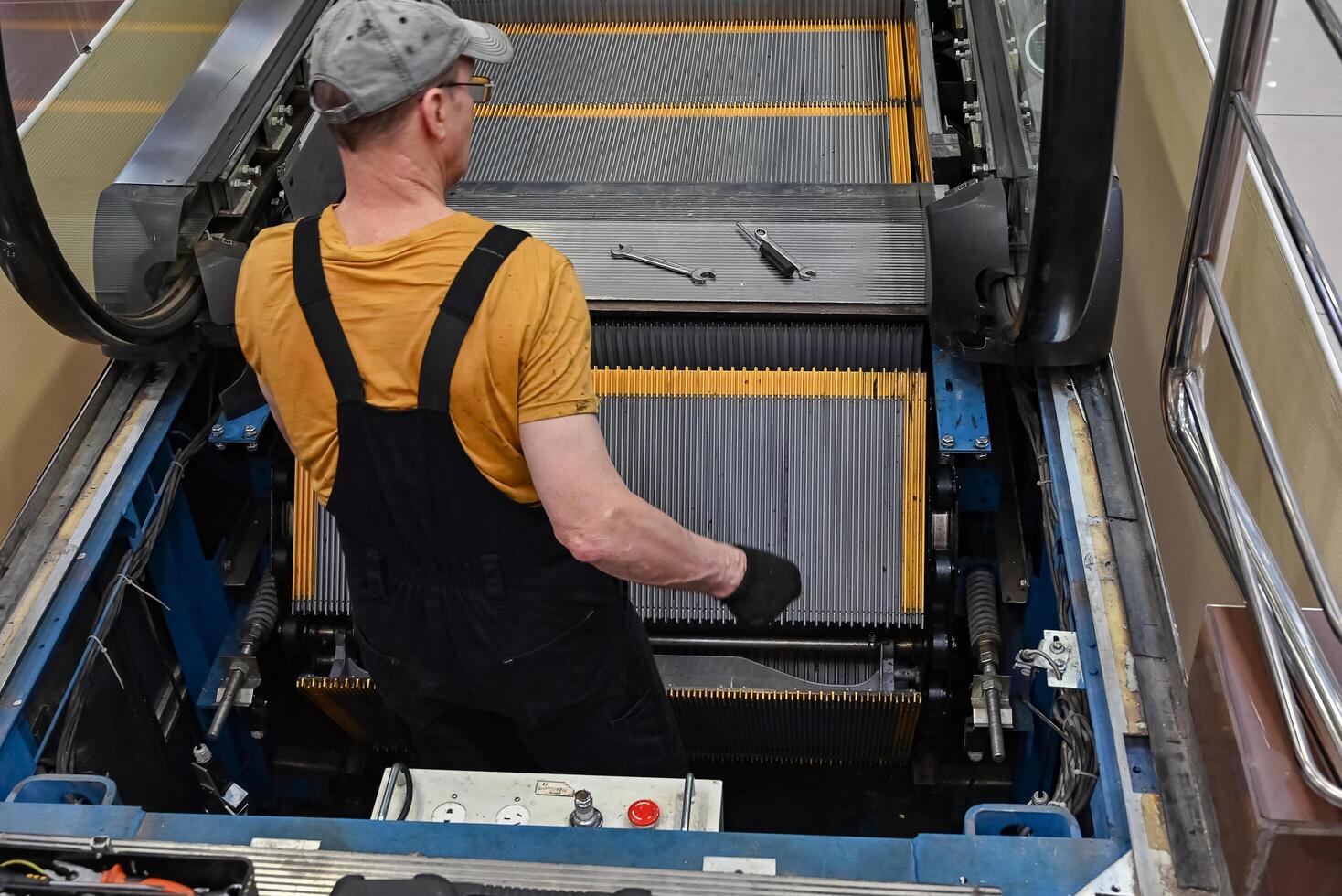 Man repairs escalator On a wonderful day with a positive attitude, steps inside, standing with her back near the step, tools are. photo