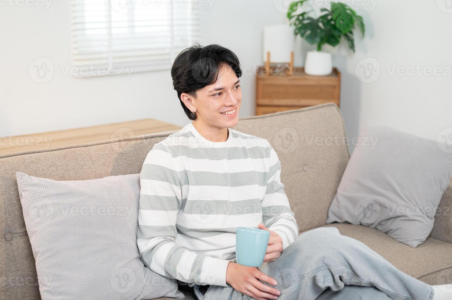 A happy Asian man enjoys his coffee on the sofa in the living room while watching the news on TV. photo