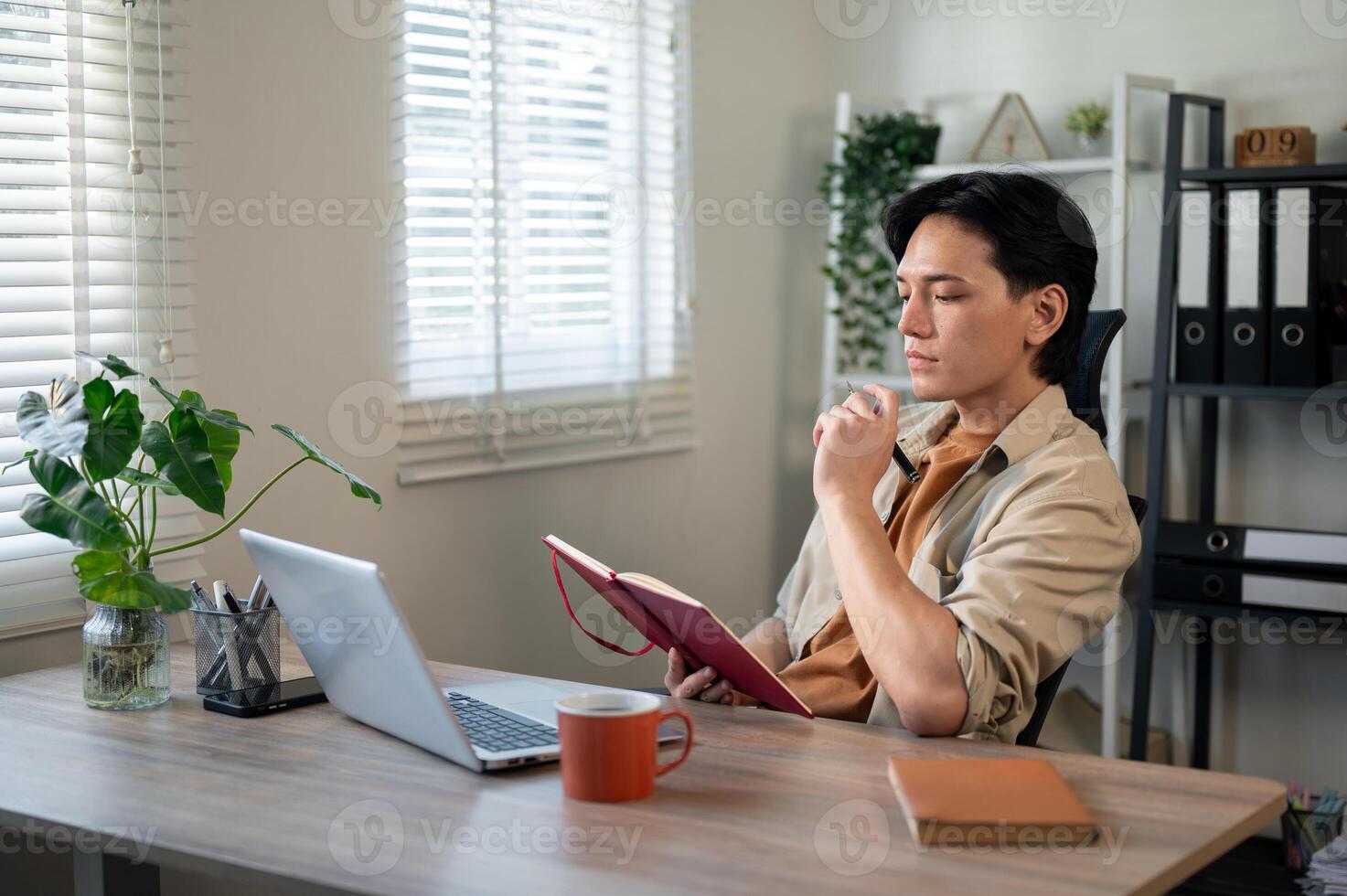A focused, smart Asian businessman is contemplating his work ideas and writing them in a book. photo