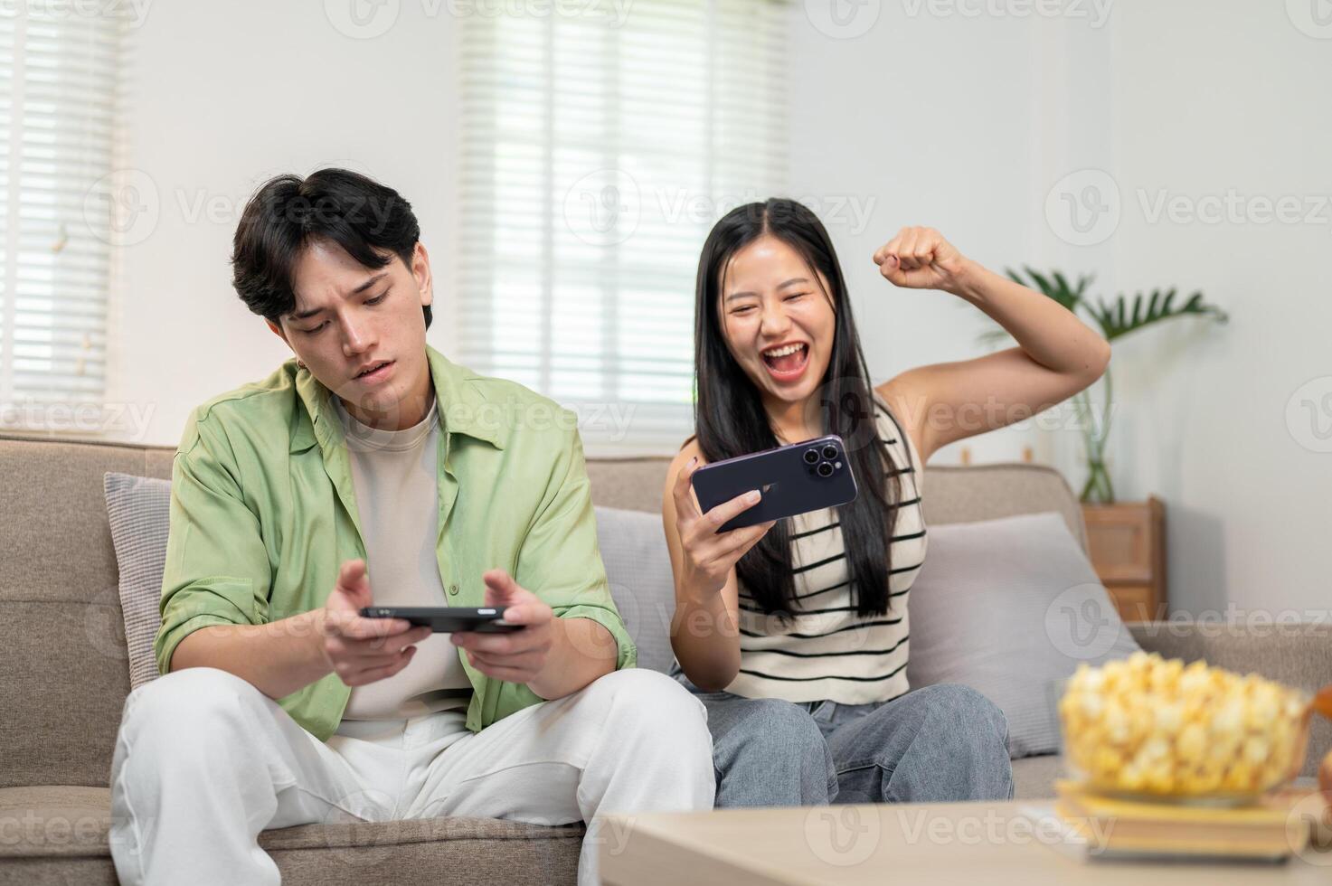 A joyful Asian couple enjoys racing a game on their smartphone, spending fun time at home together. photo