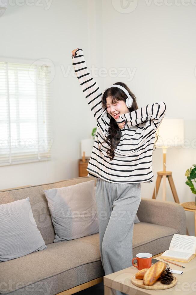 A happy young Asian woman is singing and dancing in the living room, enjoying the music. photo