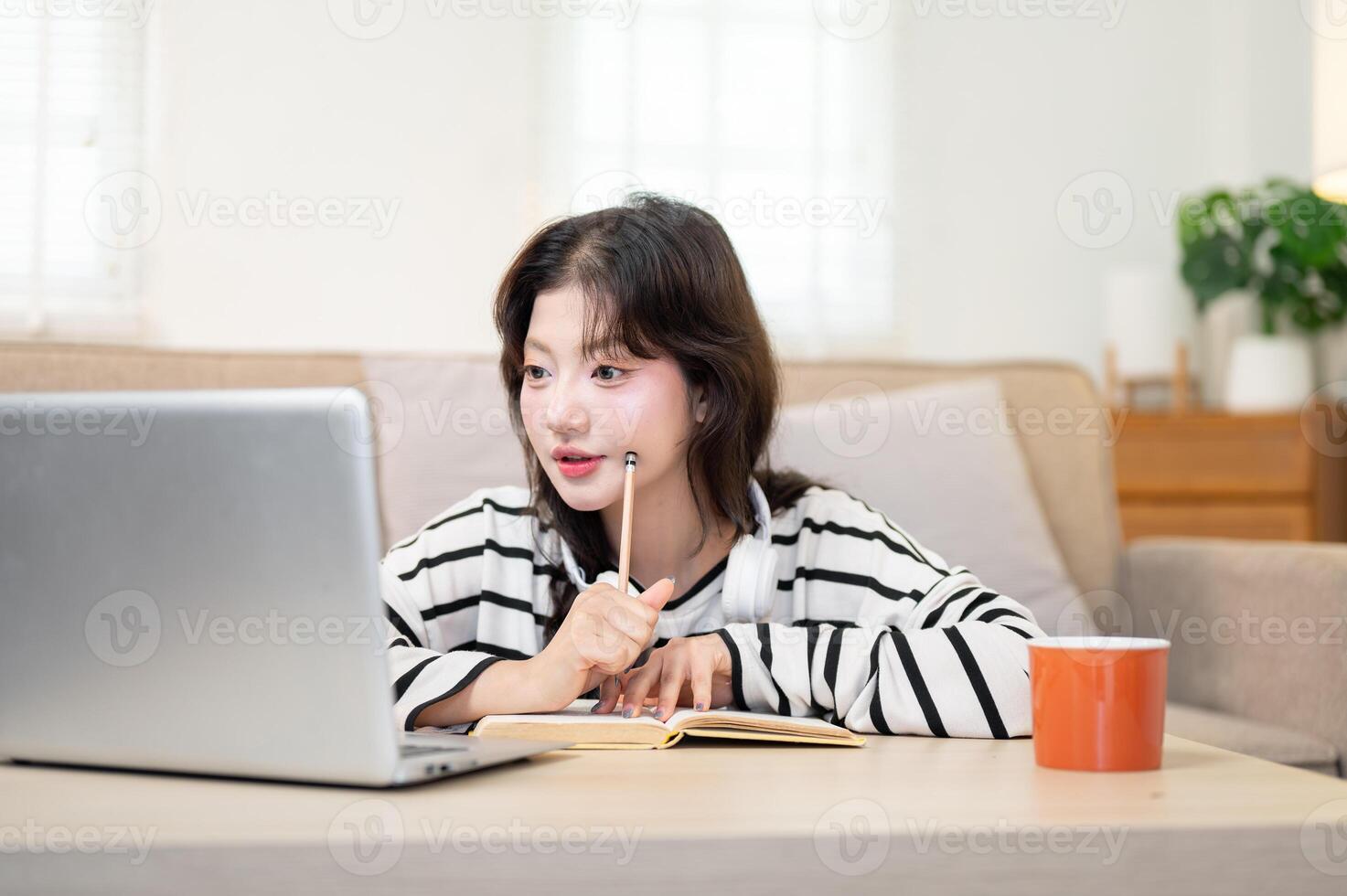 A pretty, thoughtful Asian female student is focusing on an online lecture as she studies from home. photo