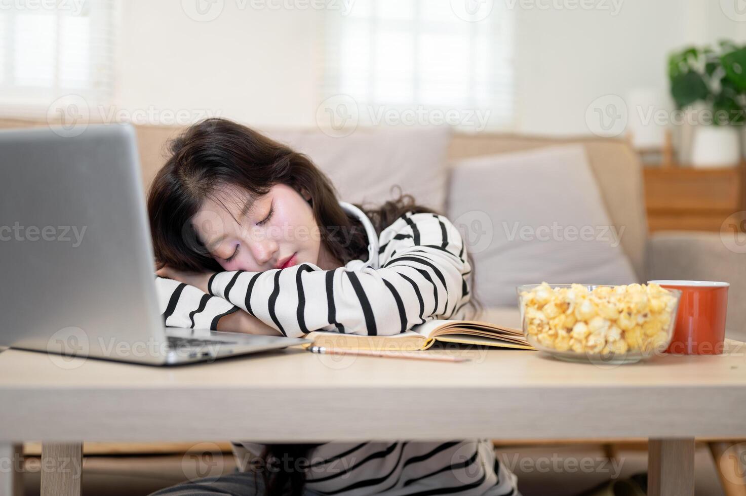 An Asian female student feeling exhausted from her online lecture, is taking a nap at a coffee table photo