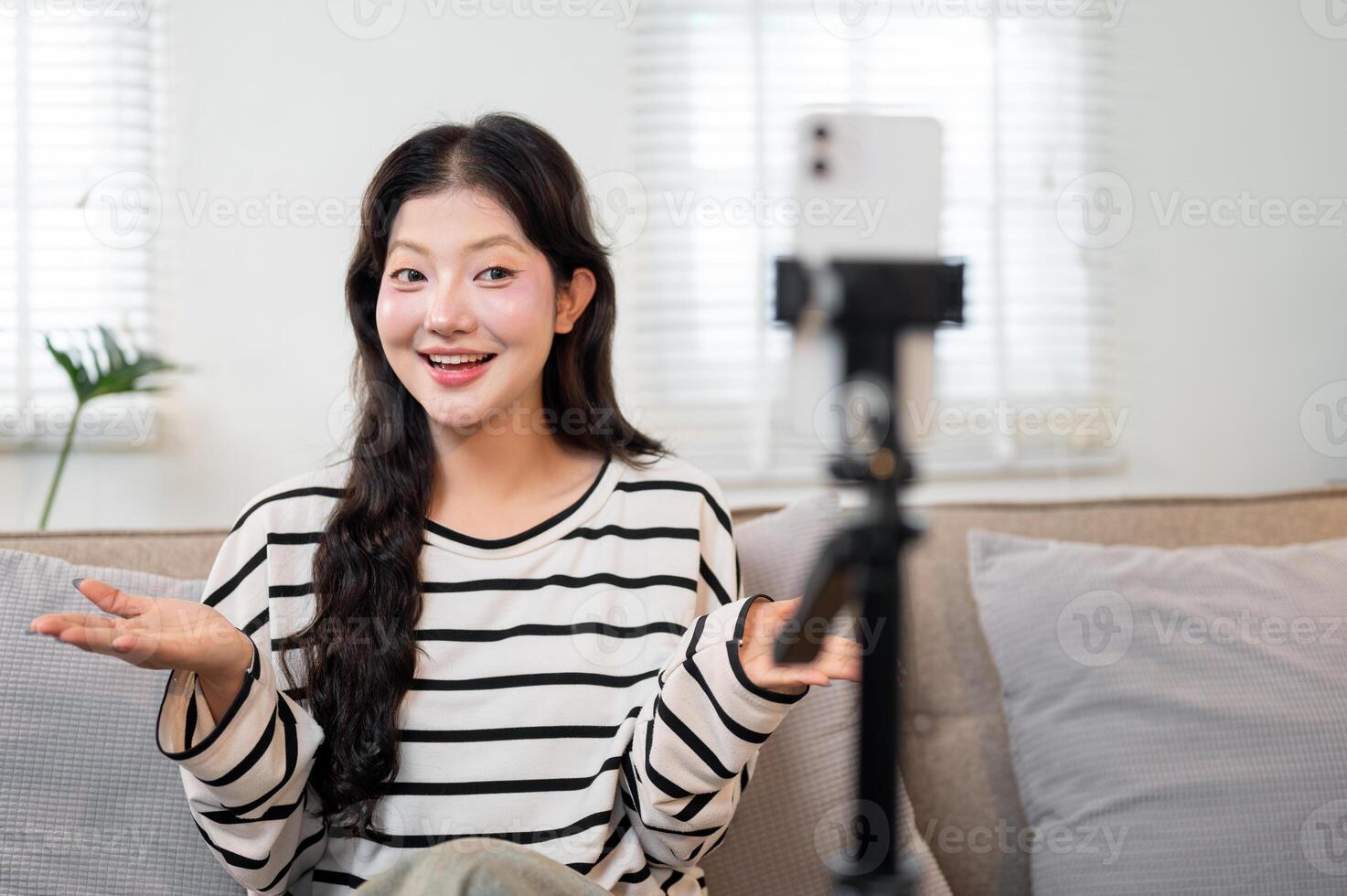 An attractive Asian female influencer sits on a sofa, recording a lifestyle from her home. photo