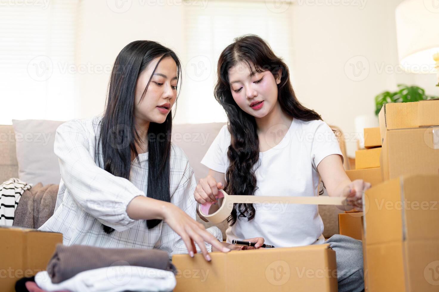 Two beautiful Asian women are helping each other pack their belongings into cardboard boxes. photo
