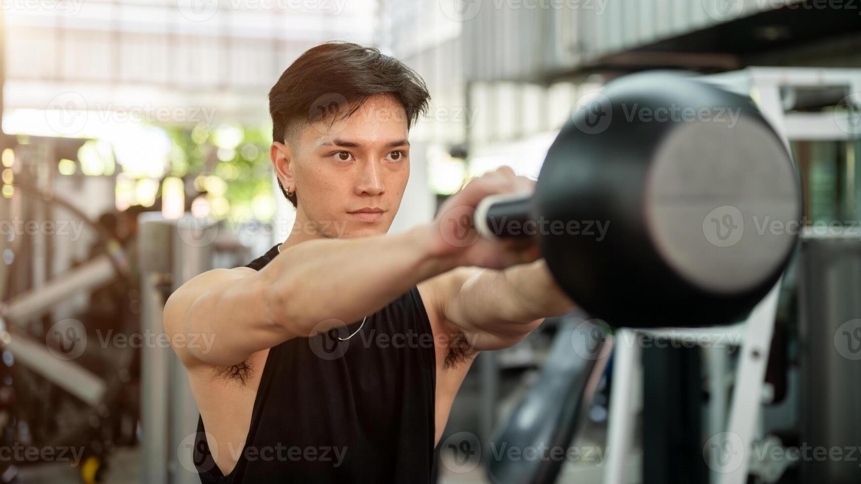 A determined and strong Asian man is working out with a kettlebell, exercising in the gym. photo