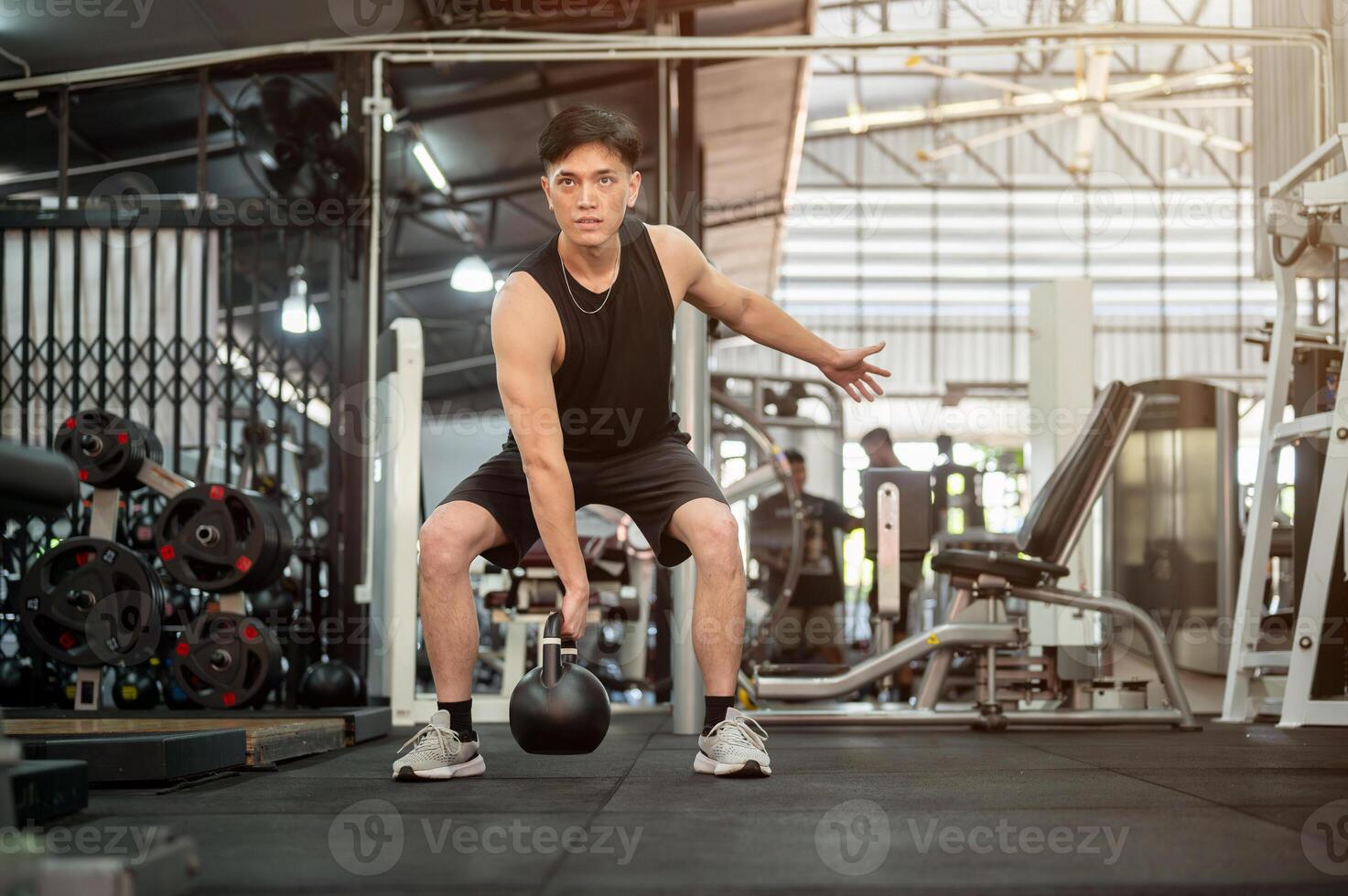 A strong Asian man is performing a squat with a kettlebell, exercising with equipment in the gym. photo