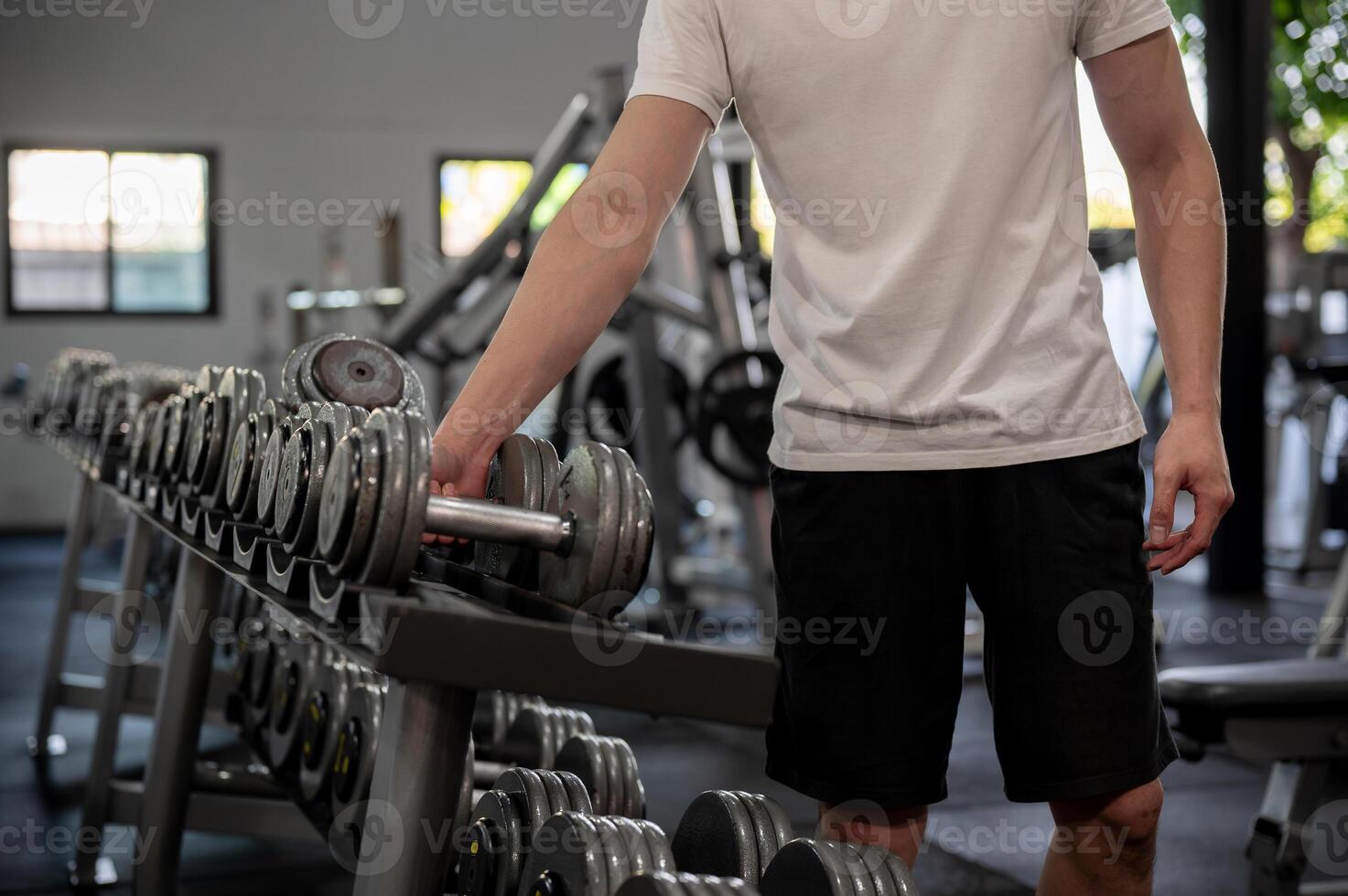 A close-up of a man is selecting a dumbbell from the rack in the gym, preparing for weight training. photo