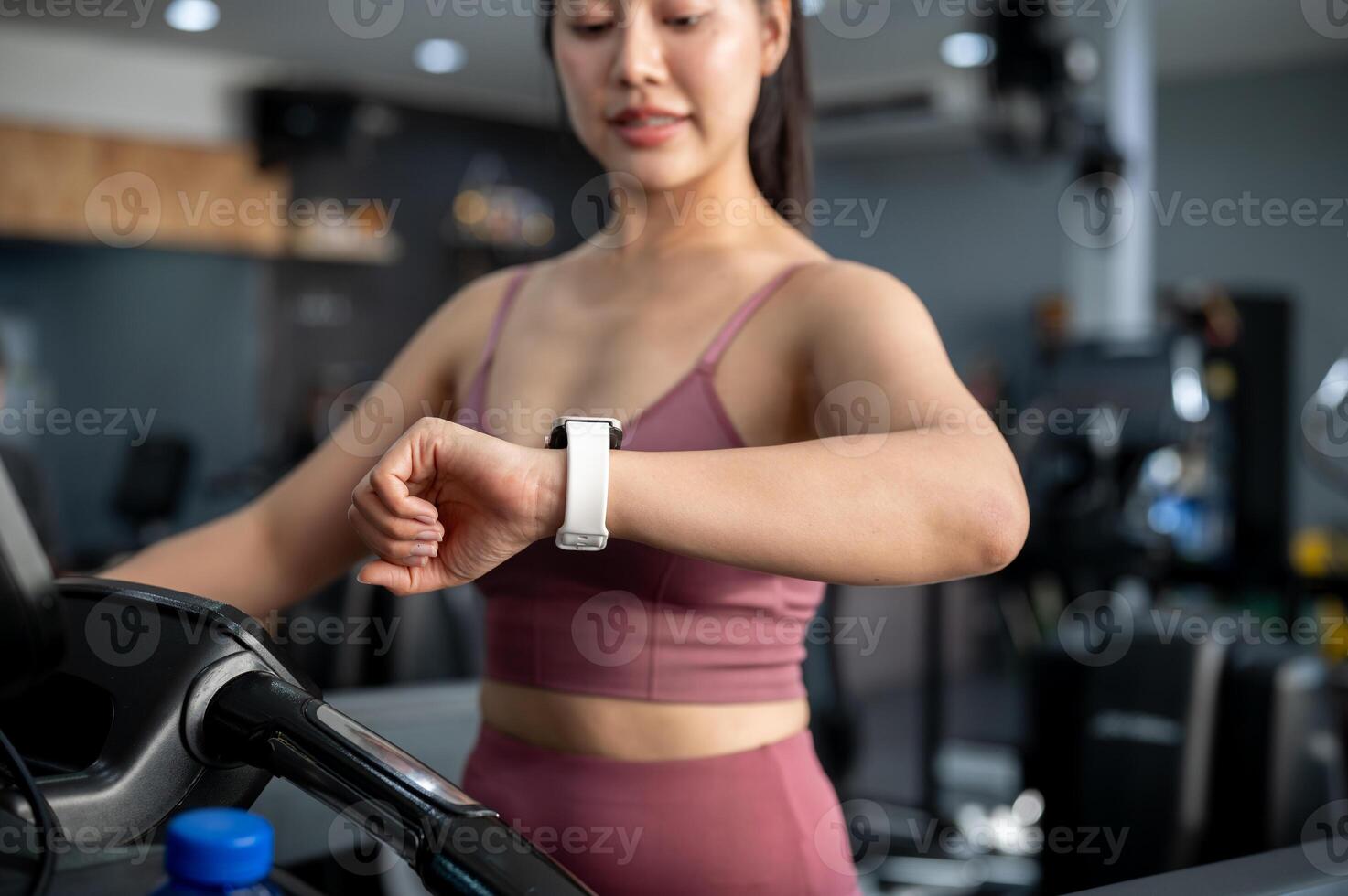 A sporty woman is checking her calorie count on her smartwatch while walking on a treadmill. photo