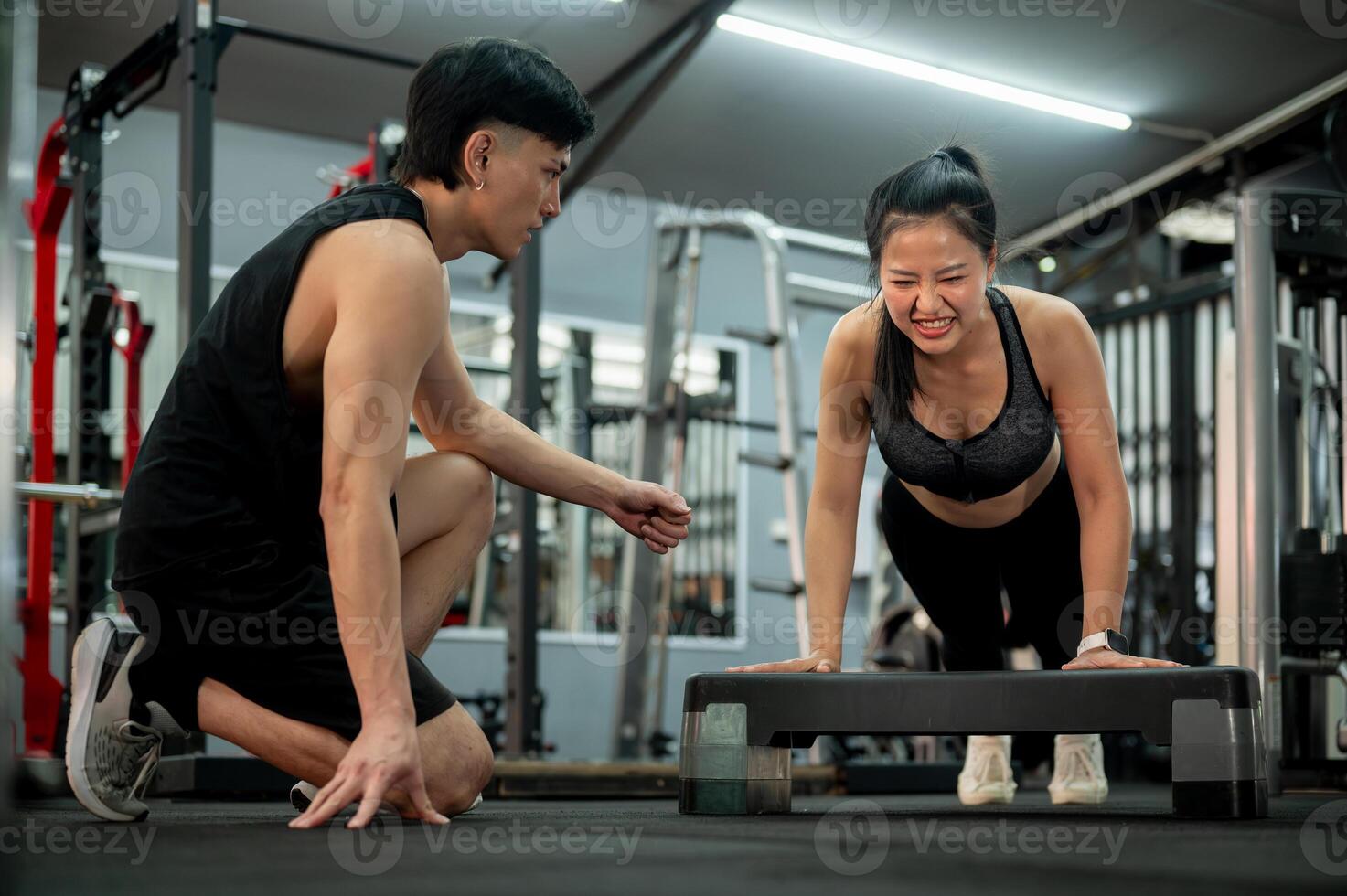 A determined Asian woman is being trained by a fitness trainer while performing push-ups. photo