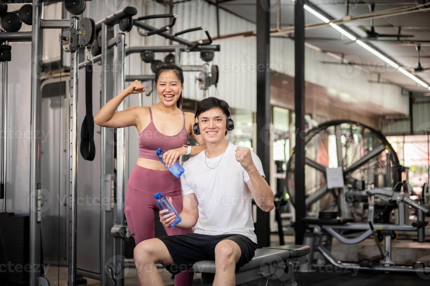 A cheerful and fit Asian people are smiling and showing a fist to the camera while standing in a gym photo