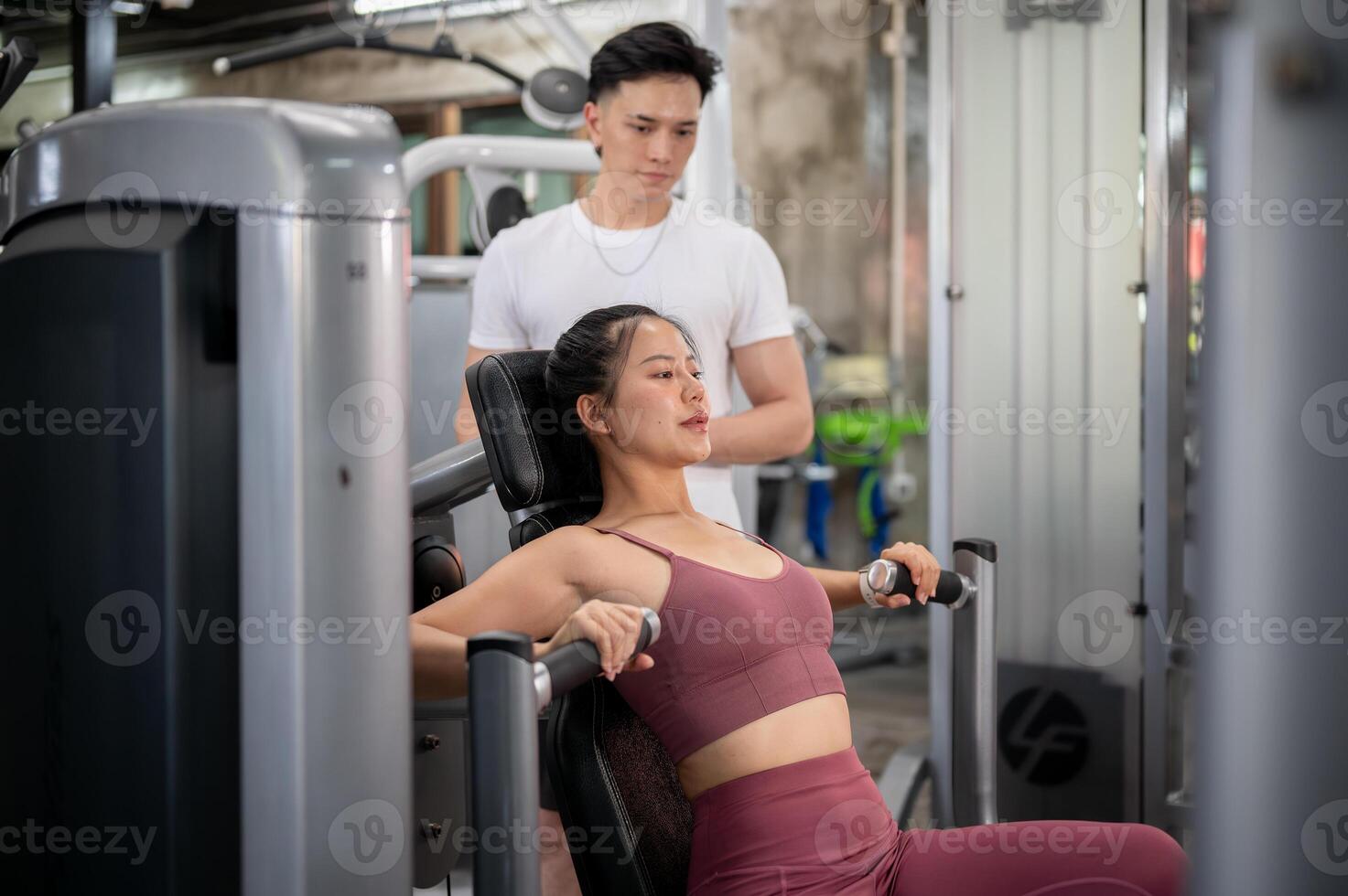 A determined and fit Asian woman in sportswear is being instructed by a professional fitness trainer photo