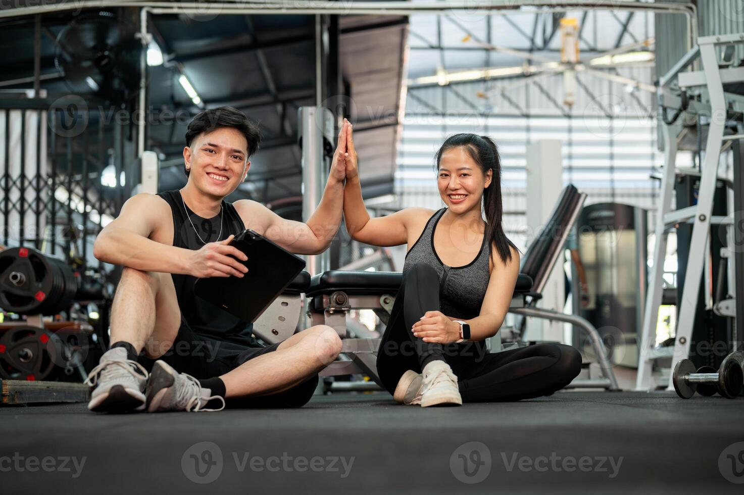 A cheerful Asian male fitness trainer and his client are in the gym, giving each other a high five. photo