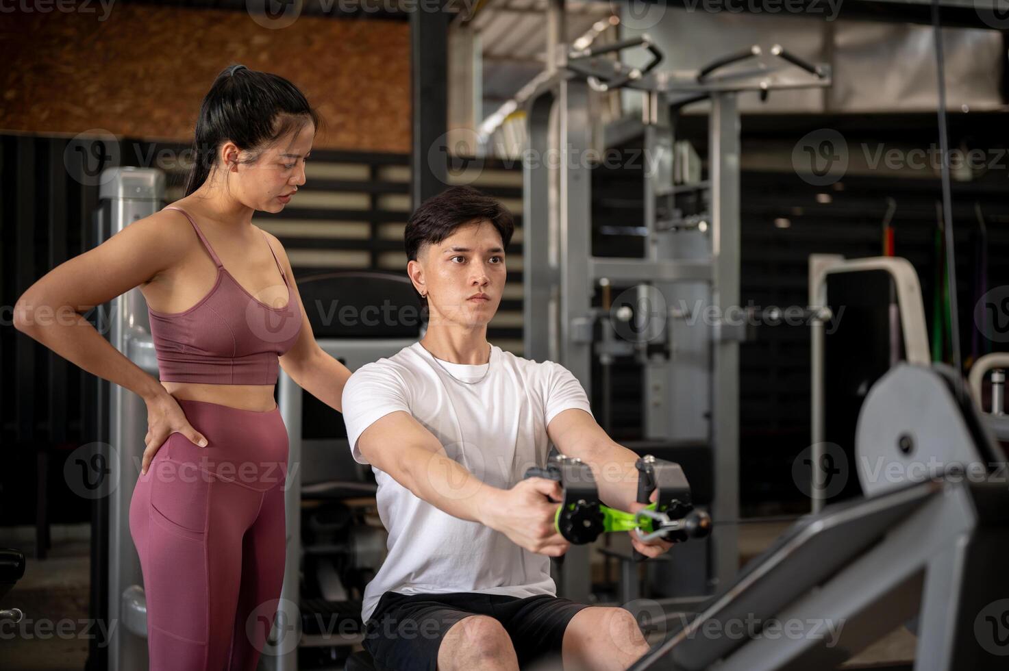 A supportive female fitness trainer is instructing a client in the gym on using the cable machine. photo