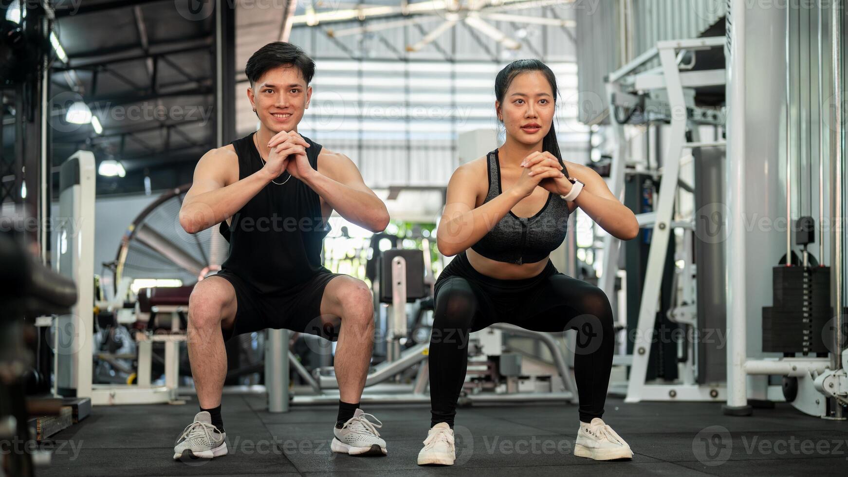 An athletic Asian couple is training together in the gym, performing squats and bodyweight exercises photo