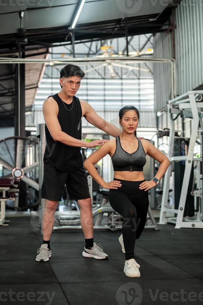 A professional Asian male fitness coach is training a female client in a gym, checking her form. photo
