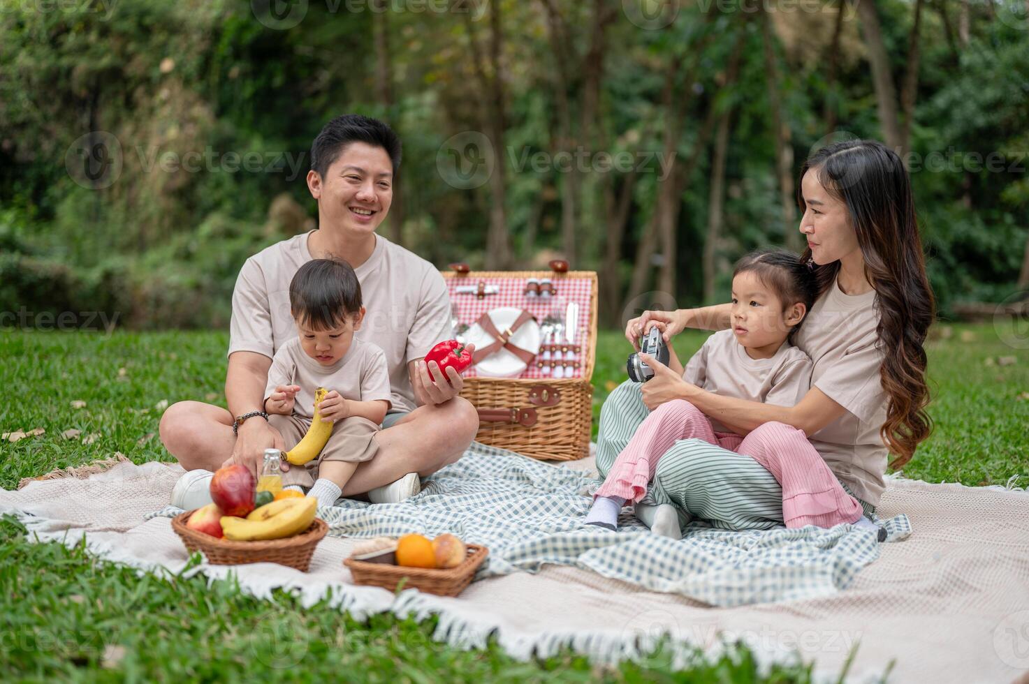 A lovely Asian family enjoys a picnic in a green park, sitting on a blanket and having fun together. photo