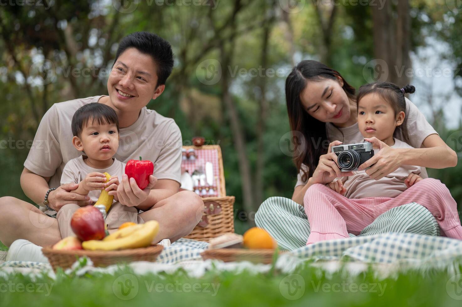 A happy Asian family enjoys a summer picnic in a park, sharing quality time with their little kids. photo
