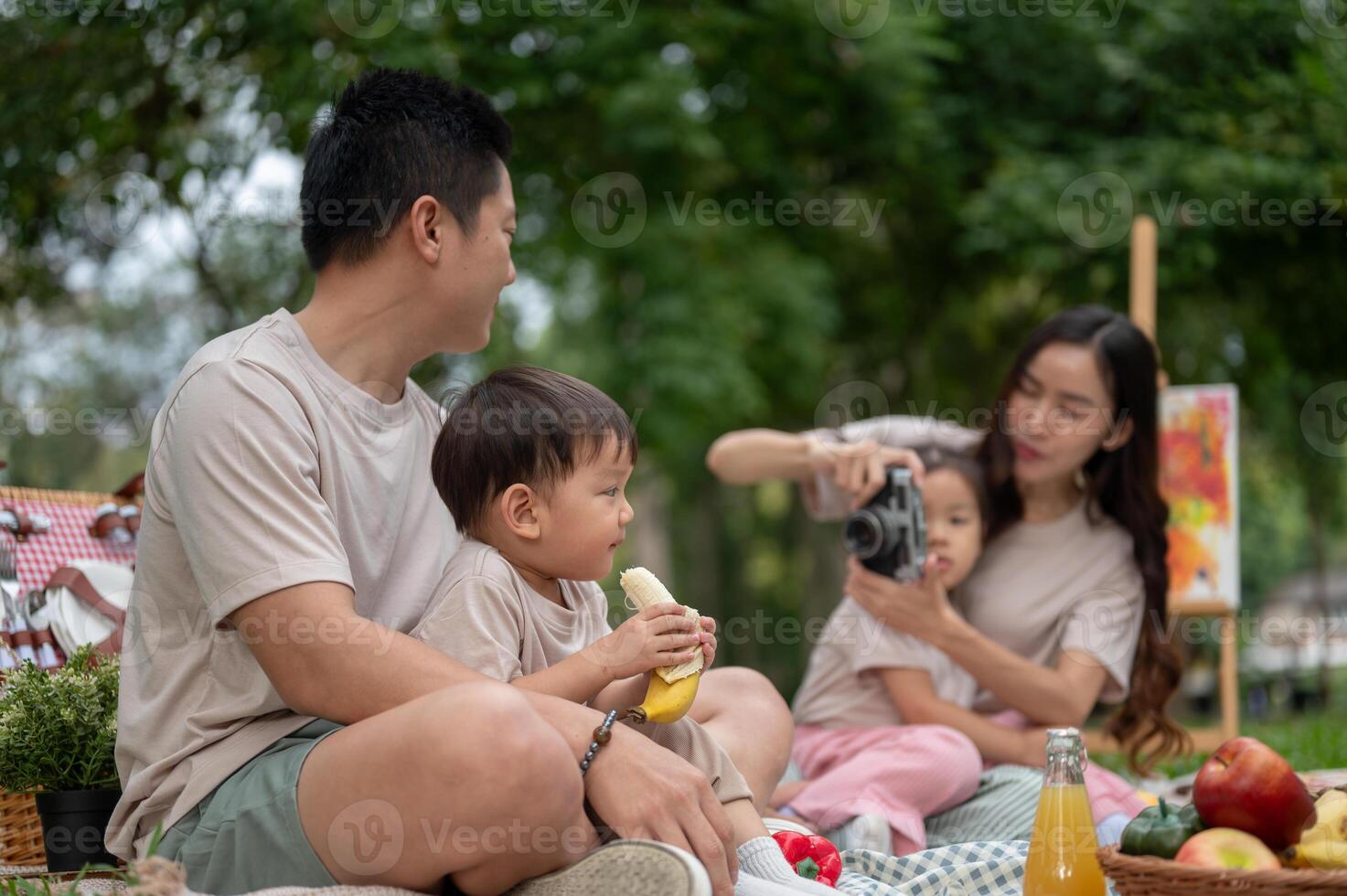 A caring Asian dad sits with his little son on his lap during a family picnic in a public park. photo