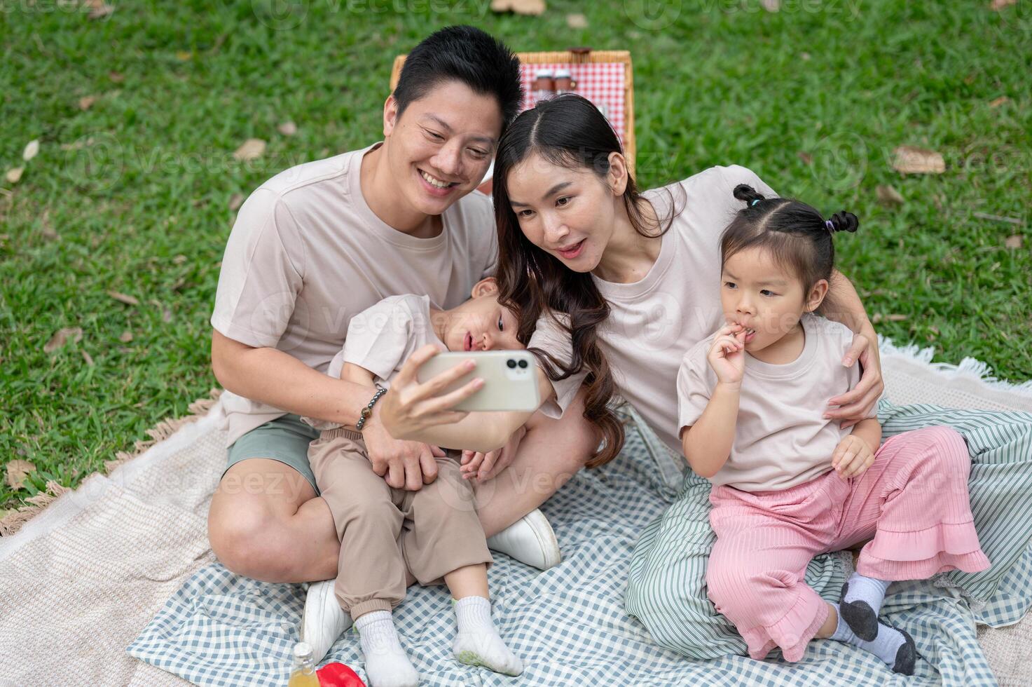 A cheerful Asian mom takes a selfie with her family during a weekend picnic in a park. photo