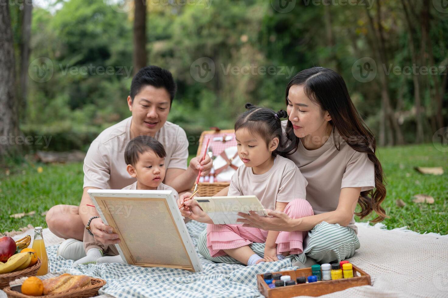 Lovely Asian parents take their little kids on a picnic in a park, enjoying painting on a canvas. photo