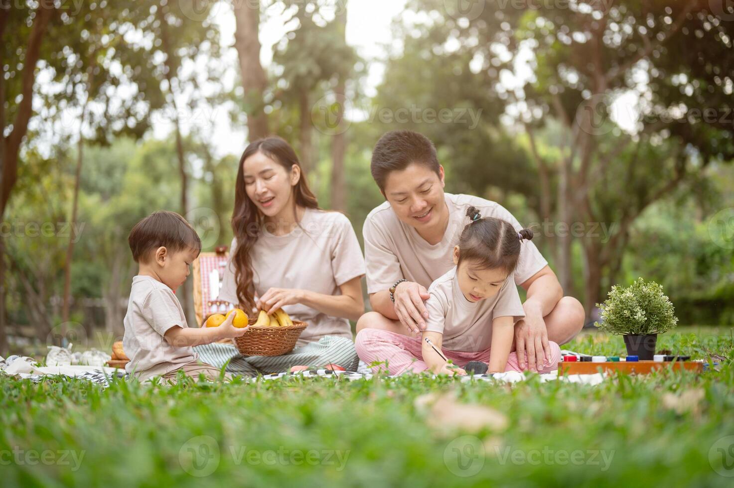 A family enjoys a picnic, dad teaching his daughter to draw while mom plays with their little boy. photo