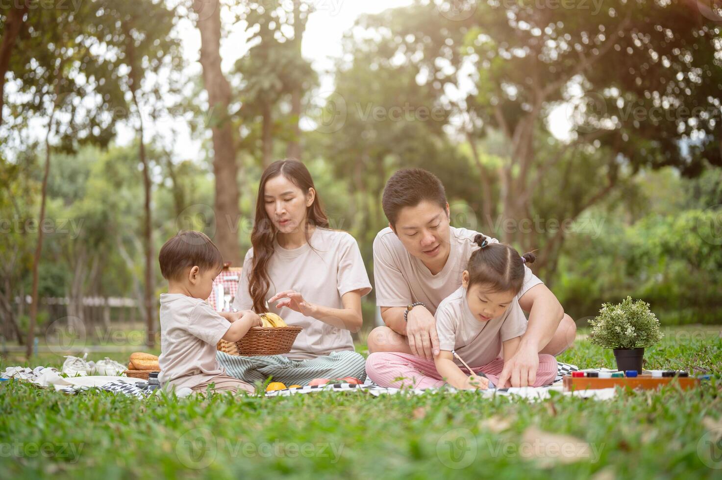 A happy Asian family enjoys a picnic in a park, with dad teaching his daughter to draw on a canvas. photo