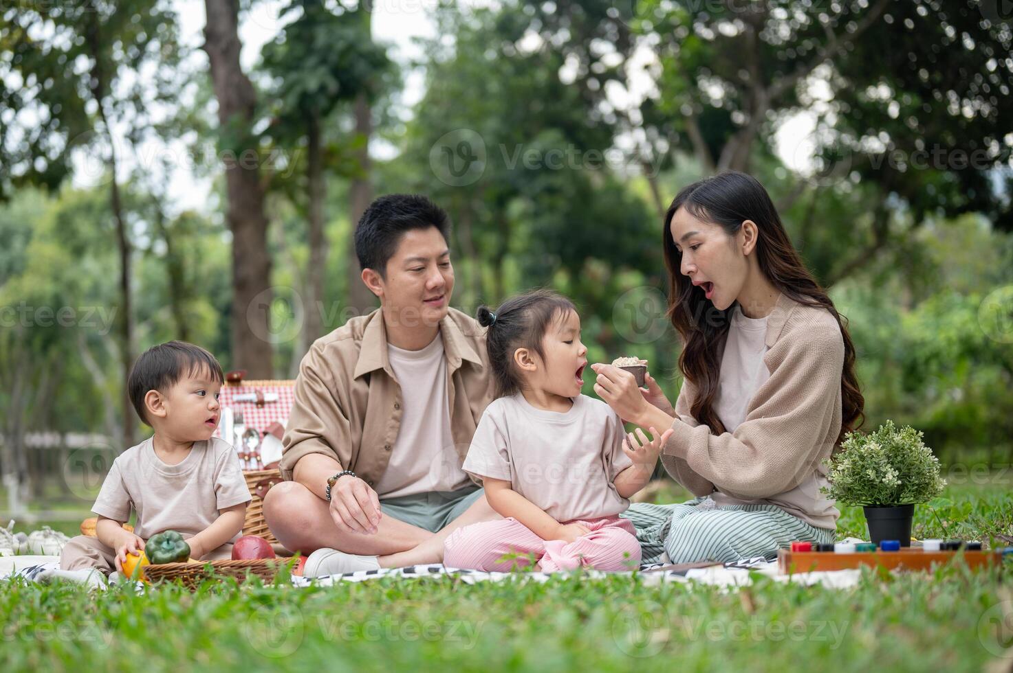 A joyful, happy Asian family picnics in a park, enjoying a conversation and eating snacks. photo