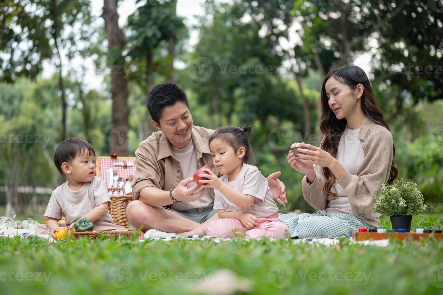 A happy Asian family picnics in a park, enjoying a conversation and eating snacks. photo