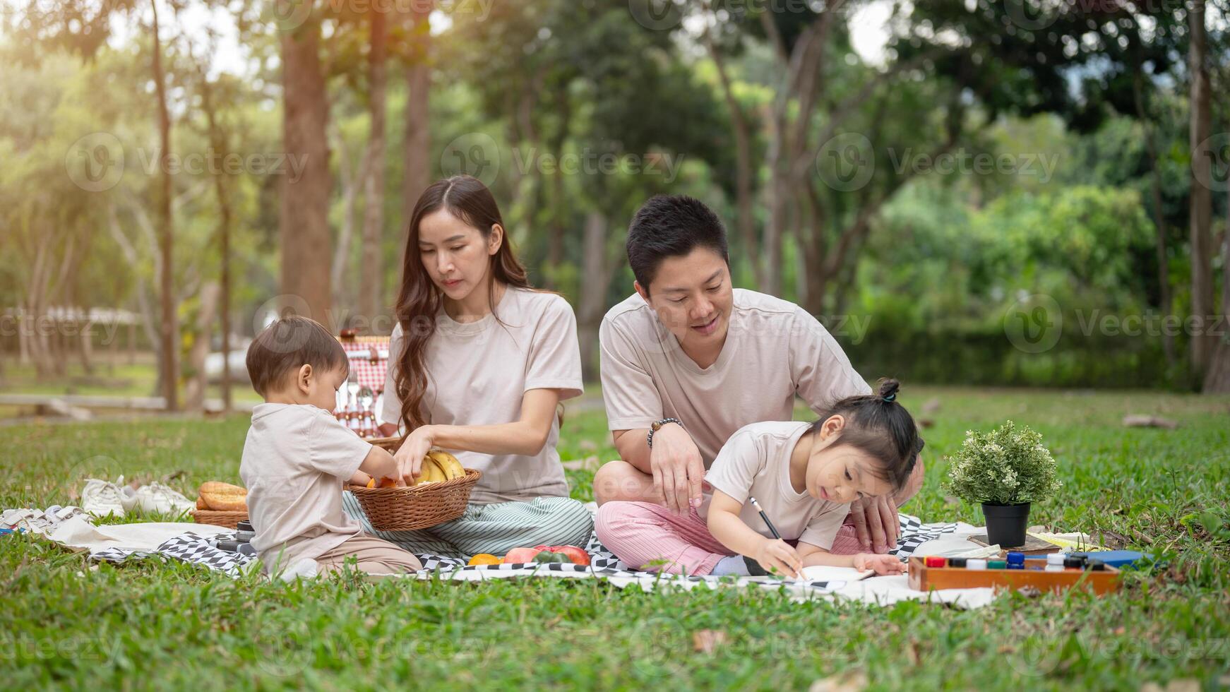A happy Asian family enjoys a picnic in a park, with dad teaching his daughter to paint on a canvas. photo