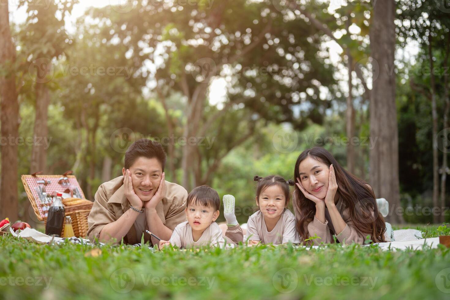 A lovely Asian family lying on a picnic blanket in a green park, smiling at the camera. photo