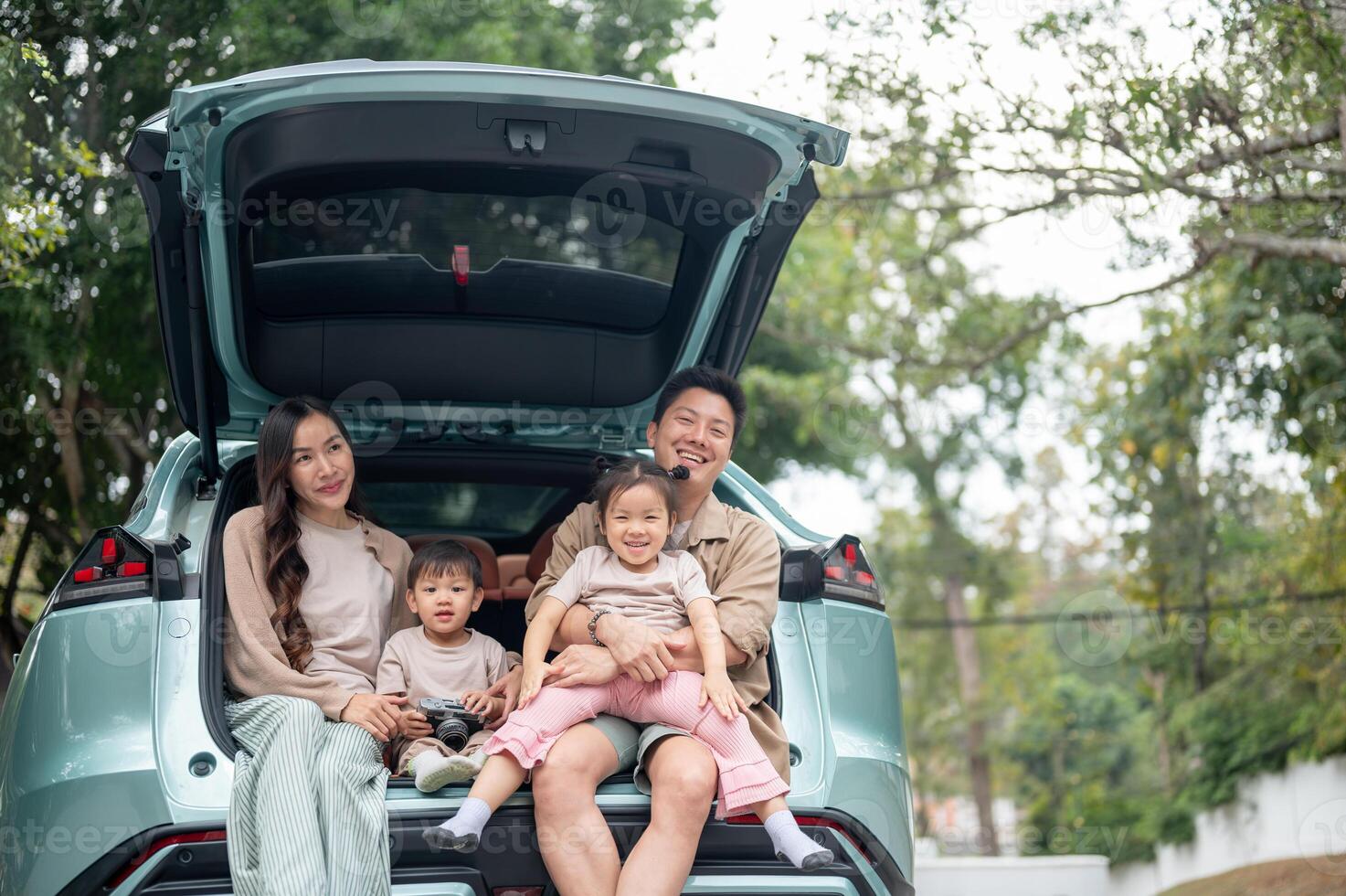 A happy Asian family sitting in the trunk of their car, enjoying their adventure together. photo