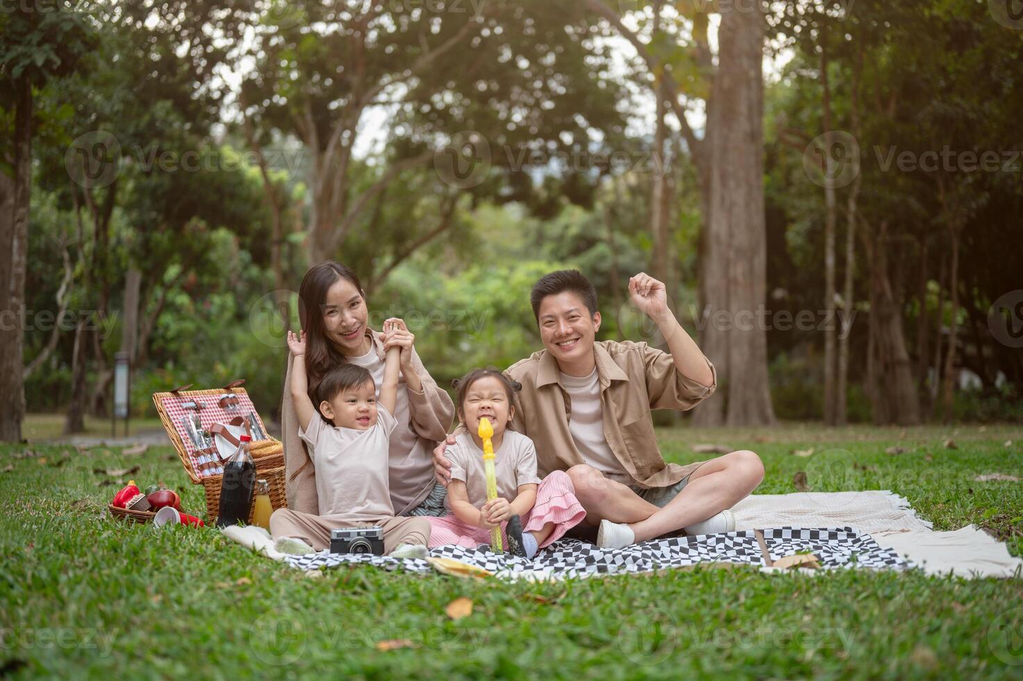 A happy, cheerful Asian family sits on a picnic blanket in a public park, smiling at the camera. photo